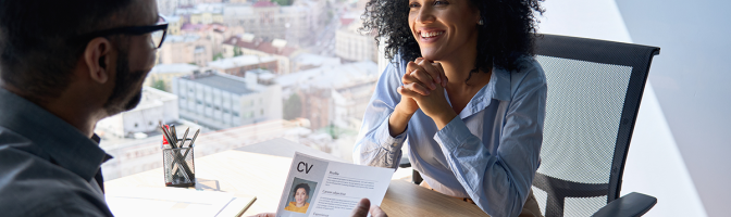 Friendly interview between businessman hr director holding resume and female applicant sitting in contemporary office.