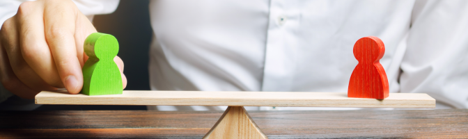 Two small wooden figures on balance scale.