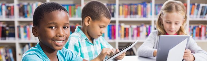 elementary school children in library using tablets and laptops on WiFi