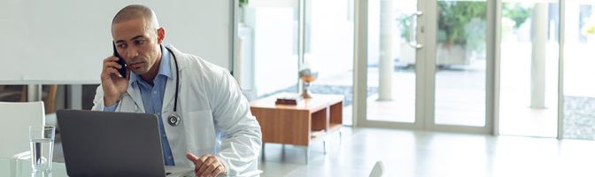 doctor talking on phone while seated in front of a labtop