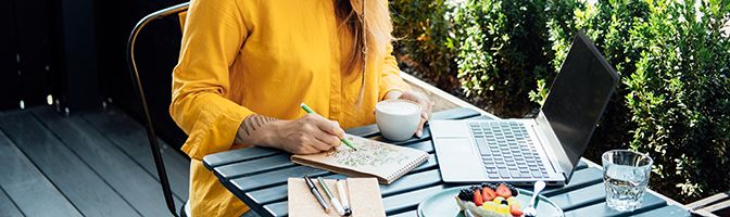 A person is coloring on a notepad while sitting at a table.