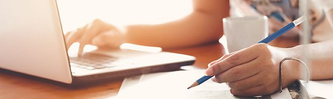 Closeup on a person with one hand on a laptop keyboard while holding a pencil in the other hand.