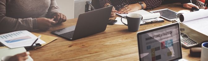 Business professionals working at table with laptops screen showing "Marketing Strategy"