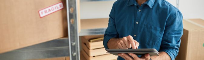 Waist up portrait of young man using digital tablet in warehouse while doing inventory and managing small business