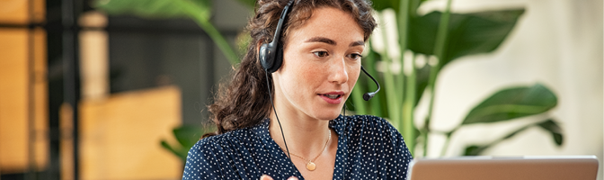 Confident young businesswoman wearing headphones conducting online meeting with colleagues.