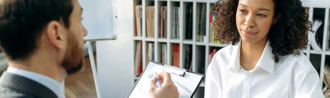 Young woman sitting at office table getting interviewed by hiring manager looking at resume.