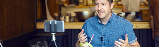 Social media influencer or food blogger creating content inside small restaurant. Man sharing online food review using smartphone on tripod. 