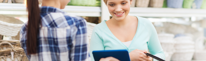 happy gardener with tablet pc helping woman with choosing flowers at flower shop