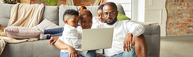 Family of four relax in their living room watching a movie through a laptop.