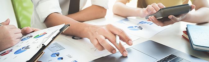 A small business team meet to discuss strategy while reviewing charts in front of a laptop..