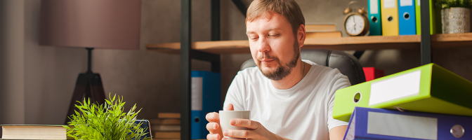 A man in the office behind a stack of folders and a laptop.