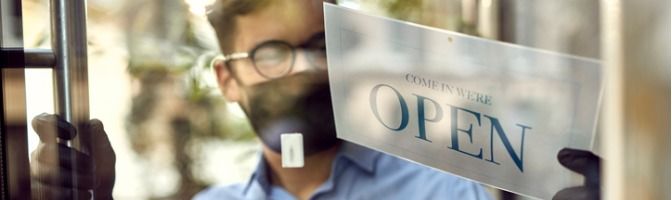 Business owner wearing a mask and gloves displays the open sign