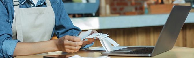 Small business owner holding receipts while sitting in front of a laptop.