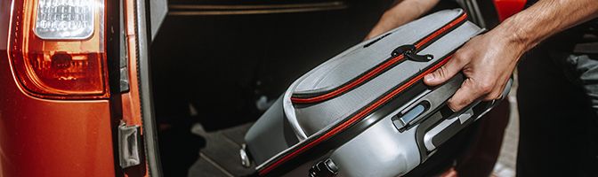 Business traveler placing luggage in the trunk of a red car.