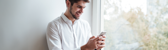 Cheerful businessman dressed in white shirt sitting and looking at phone