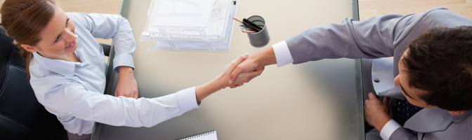 Business professionals male and female handshaking over table.