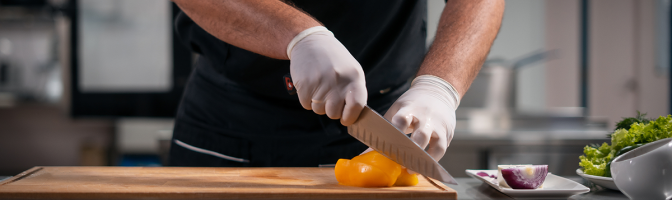 close up of chef cook hands in gloves cutting or chop yellow pepper at kitchen with knife