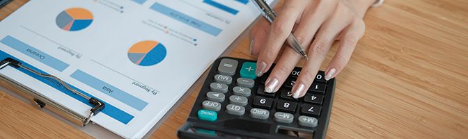 Closeup of a business owner's hand using a calculator next to a financial document.