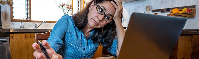 A business owner holds their head in one head while looking concerned at their laptop screen.