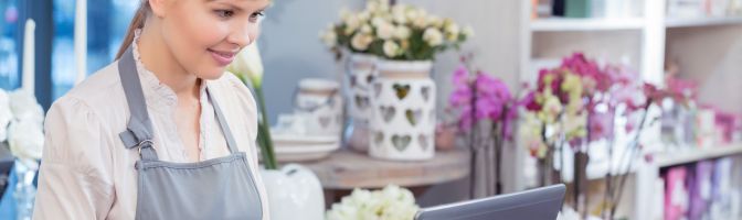 smiling woman in apron works on laptop at flower shop