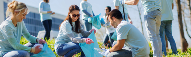 volunteering, charity, cleaning, people and ecology concept - group of happy volunteers with garbage bags cleaning area in park