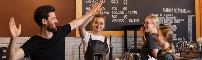 Happy male barista high fiving three female baristas in coffee shop. 