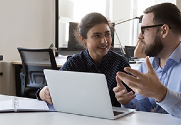 Two business professionals talking while sitting at a desk.