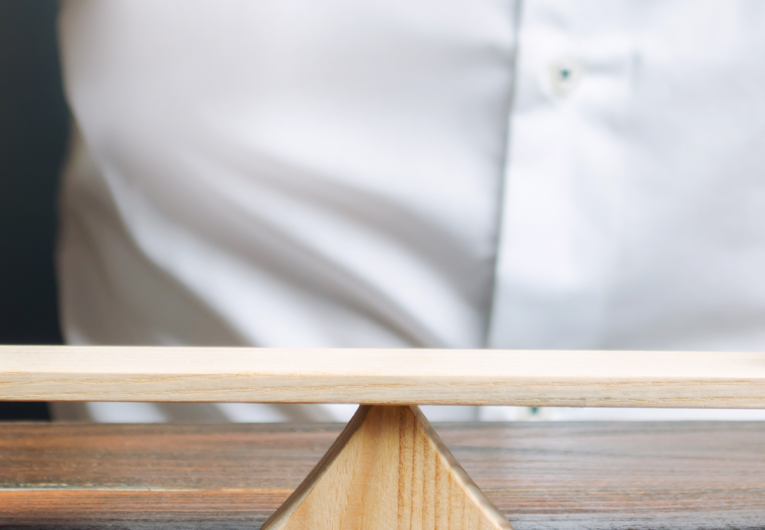 Two small wooden figures on balance scale.