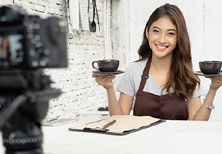 Business owner does a live stream in front of a camera in a coffee shop.