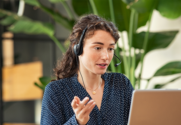 Confident young businesswoman wearing headphones conducting online meeting with colleagues.