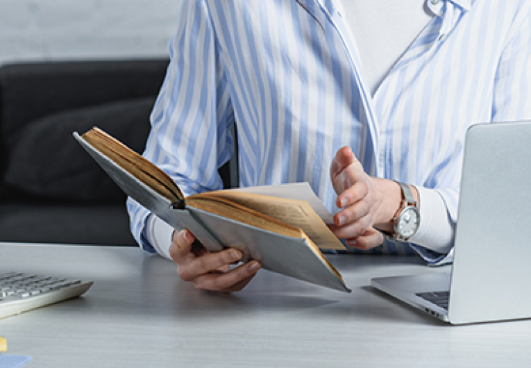 cheerful woman reading book near laptop in modern office