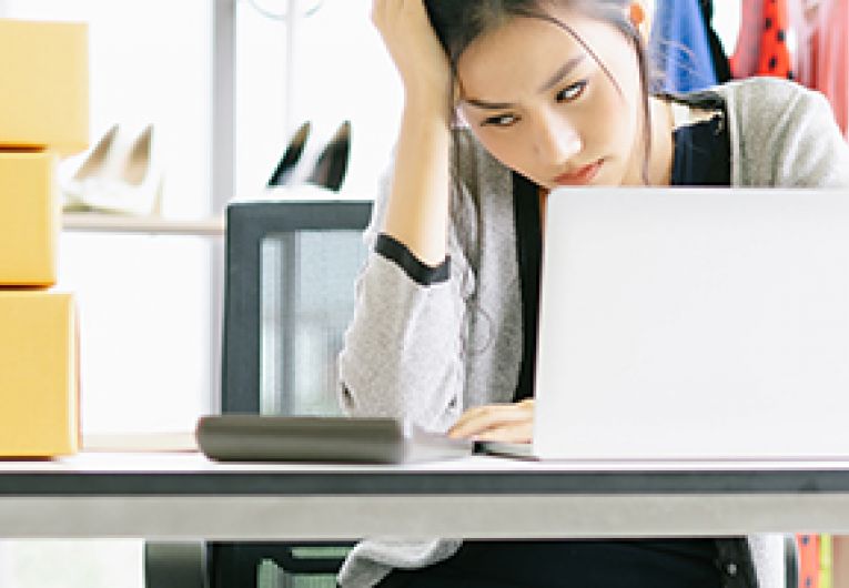 Business owner sits at a desk looking at a laptop in frustration.