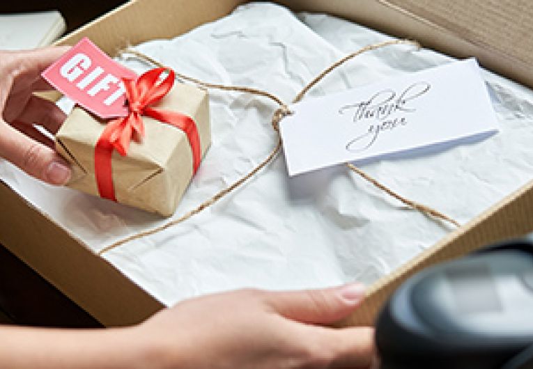 Business person prepares gift wrapped purchase for shipping in a box.