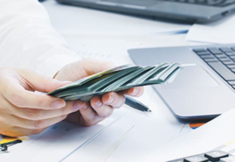 A person holding money in front of a laptop.