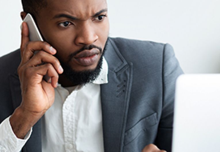 Business owner sitting in front of a laptop while holding a phone to his ear.