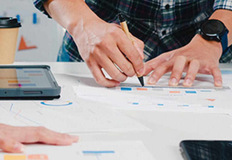 Close up of three business professionals around a table covered with print outs.