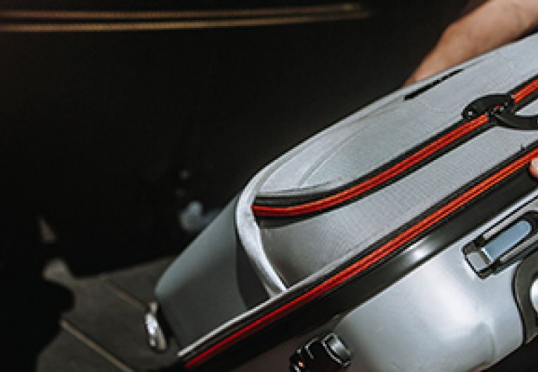 Business traveler placing luggage in the trunk of a red car.