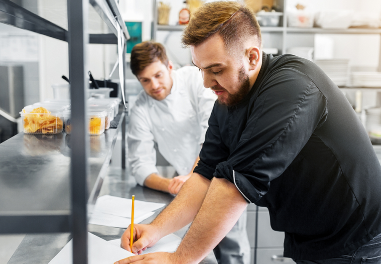 happy male chef and cook with grocery lists or bills at restaurant kitchen