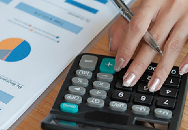 Closeup of a business owner's hand using a calculator next to a financial document.