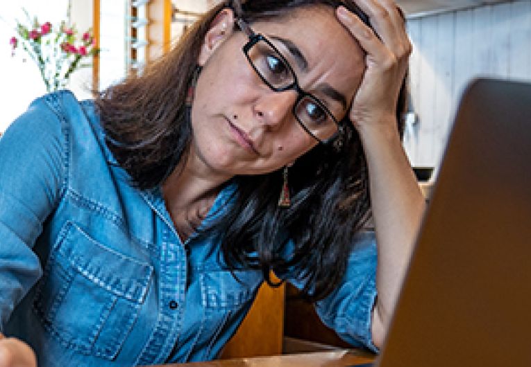 A business owner holds their head in one head while looking concerned at their laptop screen.