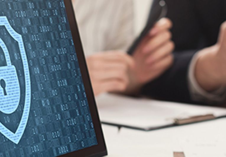 A laptop in the forefront shows a lock icon as a screensaver while two business professionals meet in thebackground.