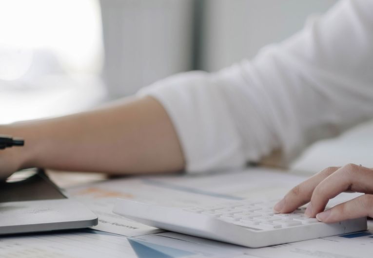 A person uses a calculator with one hand while typing on a laptop with the other.