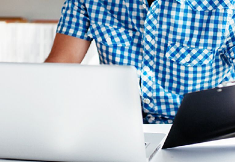 Business person with laptop reviewing clip board checklist