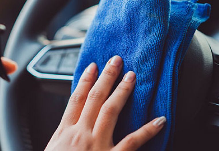 close up of someone cleaning their steering wheel with a blue rag