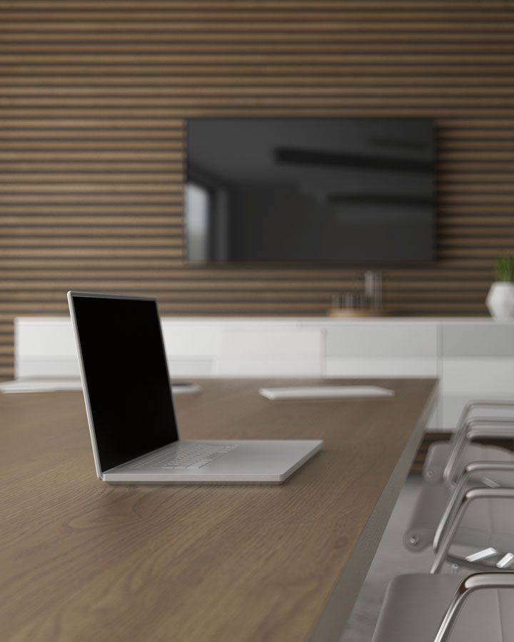 Laptop sitting on a conference table with a television in the background