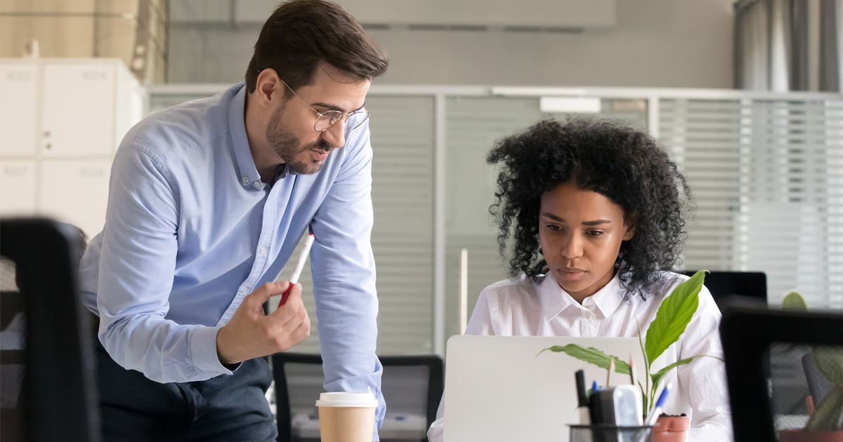 Business owner mentoring employee while they work on computer laptop