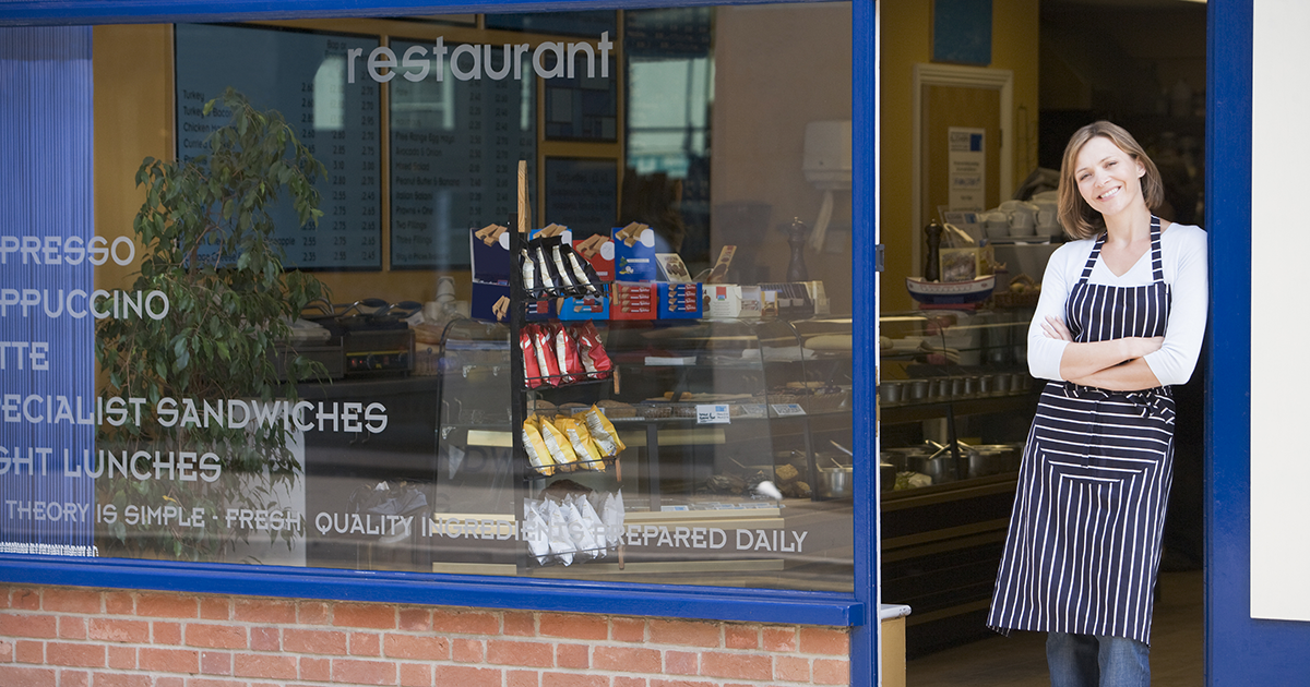 Female business owner, shop worker, standing in front of restaurant storefront. 